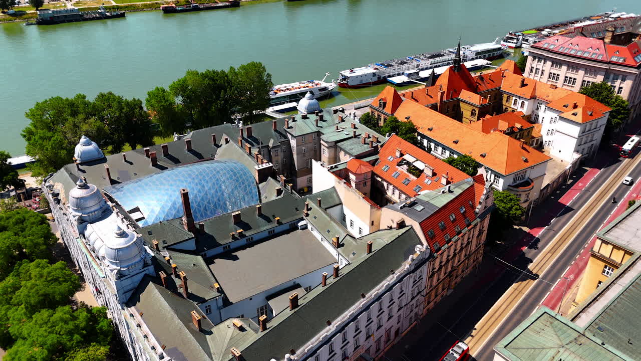 Beautiful historical buildings with grey and orange roofs. A tram moves by the straight street of Bratislava, Slovakia.