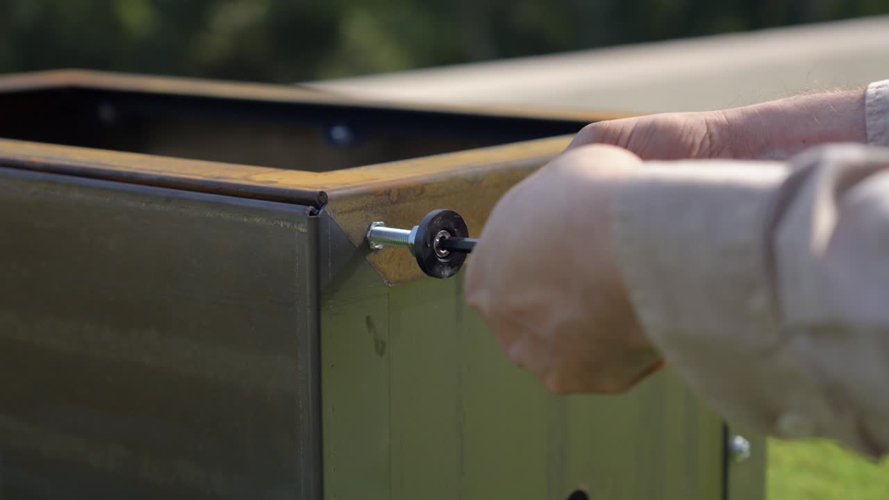 close-up of Caucasian man's hands screwing a bolt into a metal plate outdoors on a sunny day