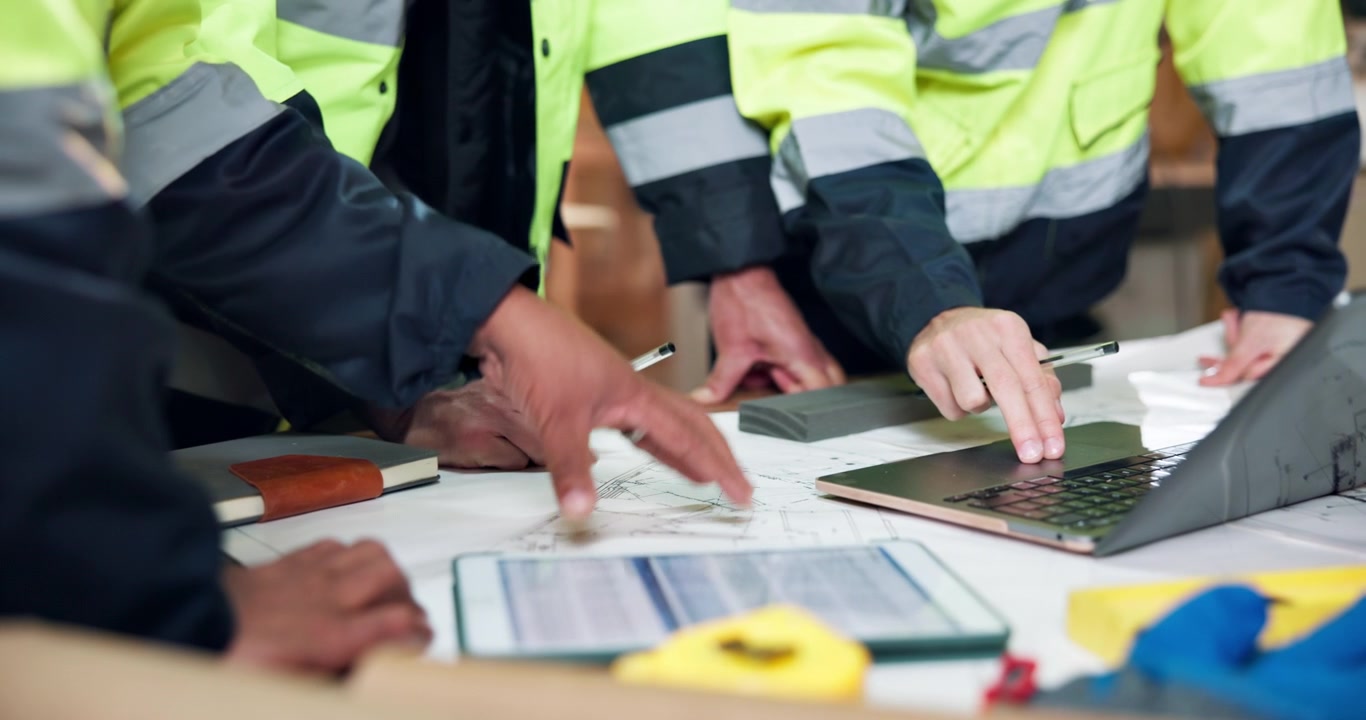 Construction Workers Reviewing Blueprints and Laptop in Office