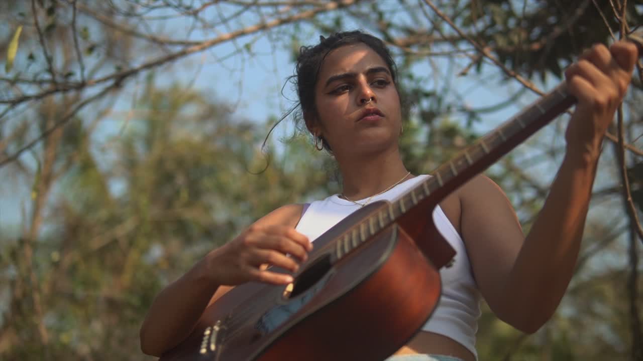 chica morena tocando una guitarra en un escenario con árboles
