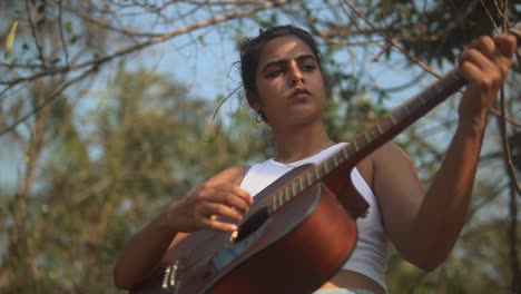 brunette girl playing a guitar on a stage with trees