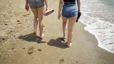 two girls walk along the sandy shorline of la cala de mijas beach on the costa del sol, leaving footprints in the sand