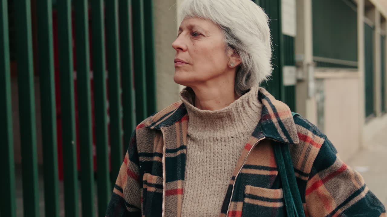 Thoughtful Senior Woman Standing by a Green Fence Outdoors