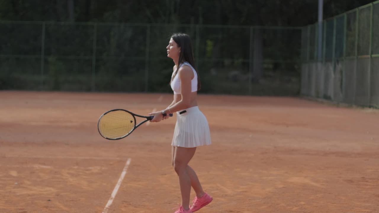 코치와 함께 야외 코트에서 테니스를 연습하는 젊은 여성. 코치는 선수가 그녀의 기술에 대해 일하면서, 운동 훈련 세션에서 그녀의 스트로크를 완성하는 동안 지침을 제공합니다.