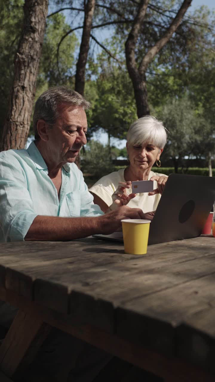 Pareja sénior comprando online en un pícnic al aire libre