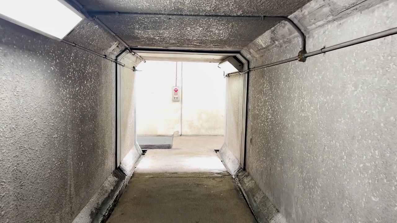Prospettiva in prima persona che si muove attraverso uno stretto tunnel di cemento con illuminazione artificiale e texture industriali.