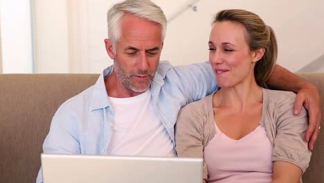 una pareja feliz usando una computadora portátil juntos en el sofá