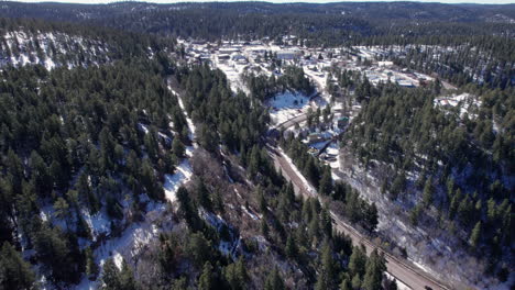 Drone-aerial-of-a-snowy-mountain-highway-with-traffic,-cars-drive-along-a-coniferous-forest