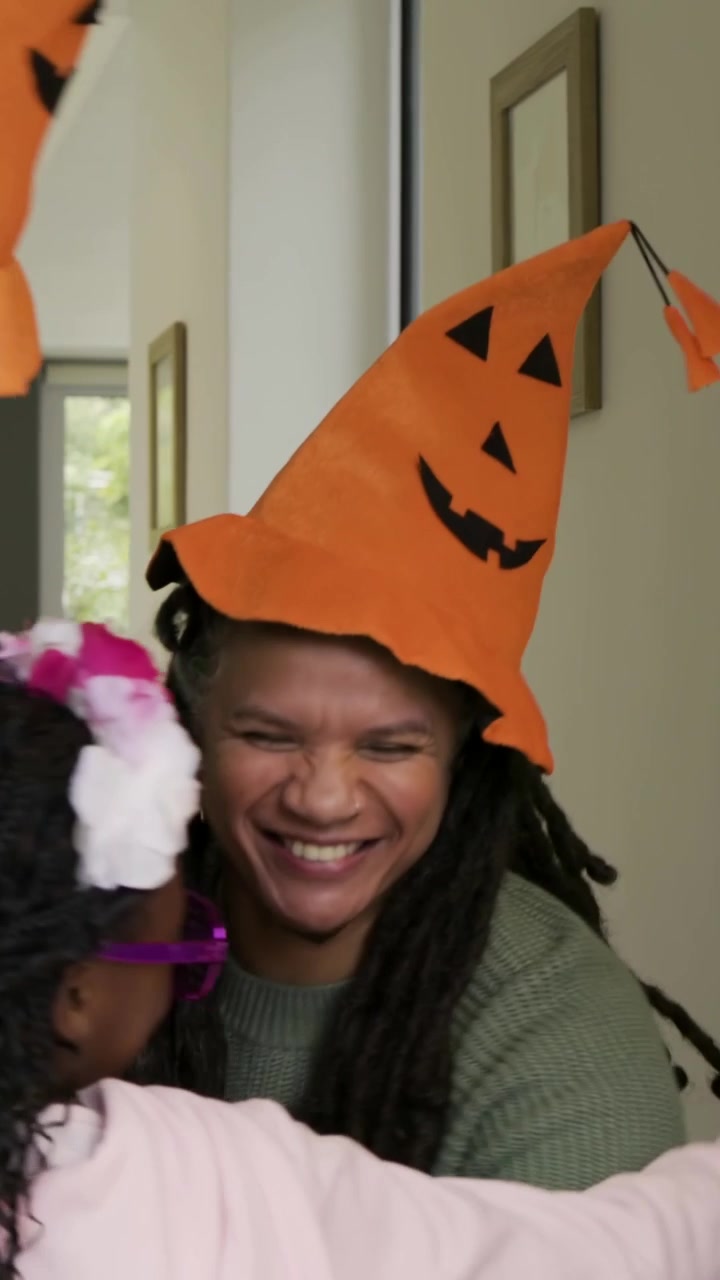 Video verticale: Adulti con cappelli a forma di zucca offrono caramelle, un bambino con felpa rosa prende un lecca-lecca alla porta.