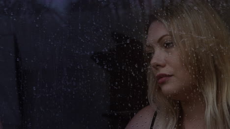 una mujer rubia solitaria mirando por la ventana a la lluvia