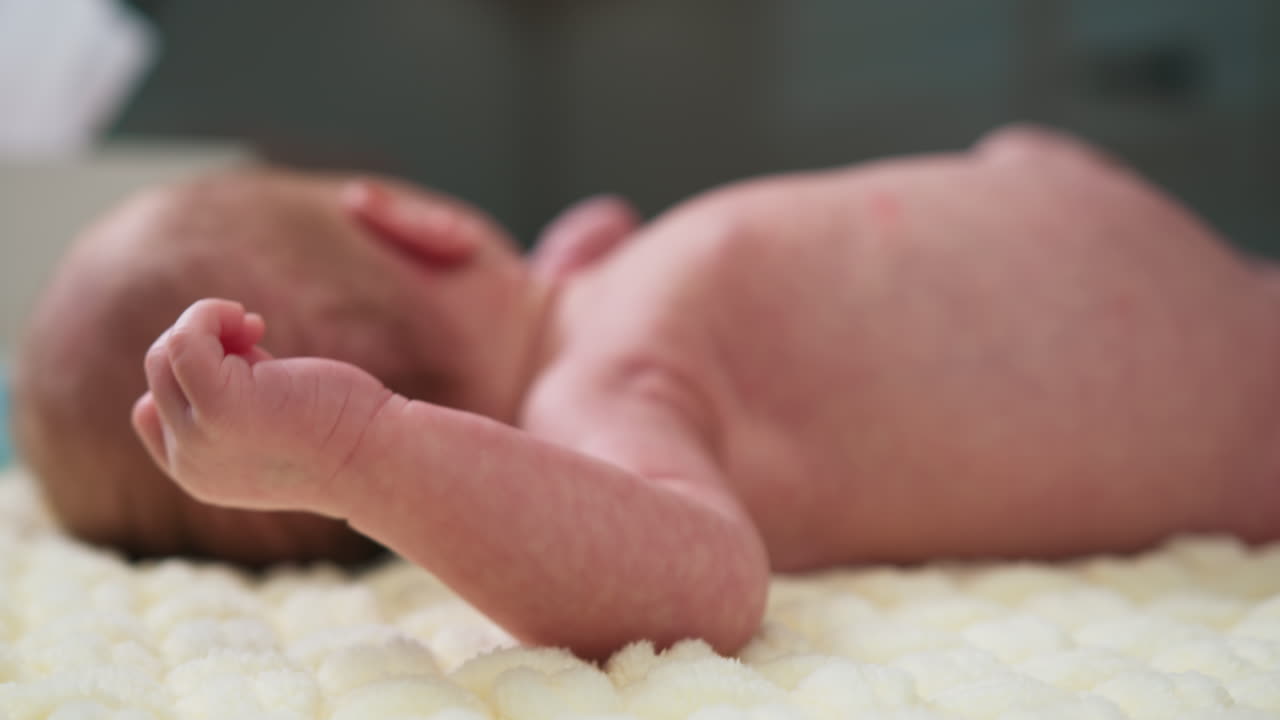 Primer plano del brazo y la mano de un bebé recién nacido descansando sobre una manta suave, mostrando su delicada piel y sus dedos.