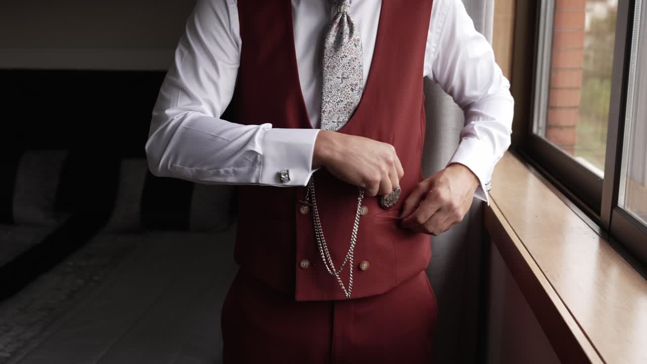 Close up groom in formal vest holding vintage pocket watch by window light
