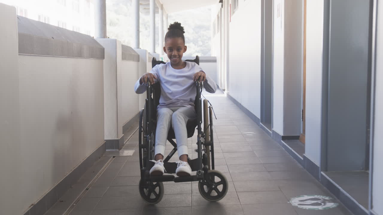 Smiling African American girl in wheelchair moving through school hallway, enjoying her day