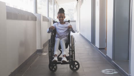 smiling african american girl in wheelchair moving through school hallway, enjoying her day