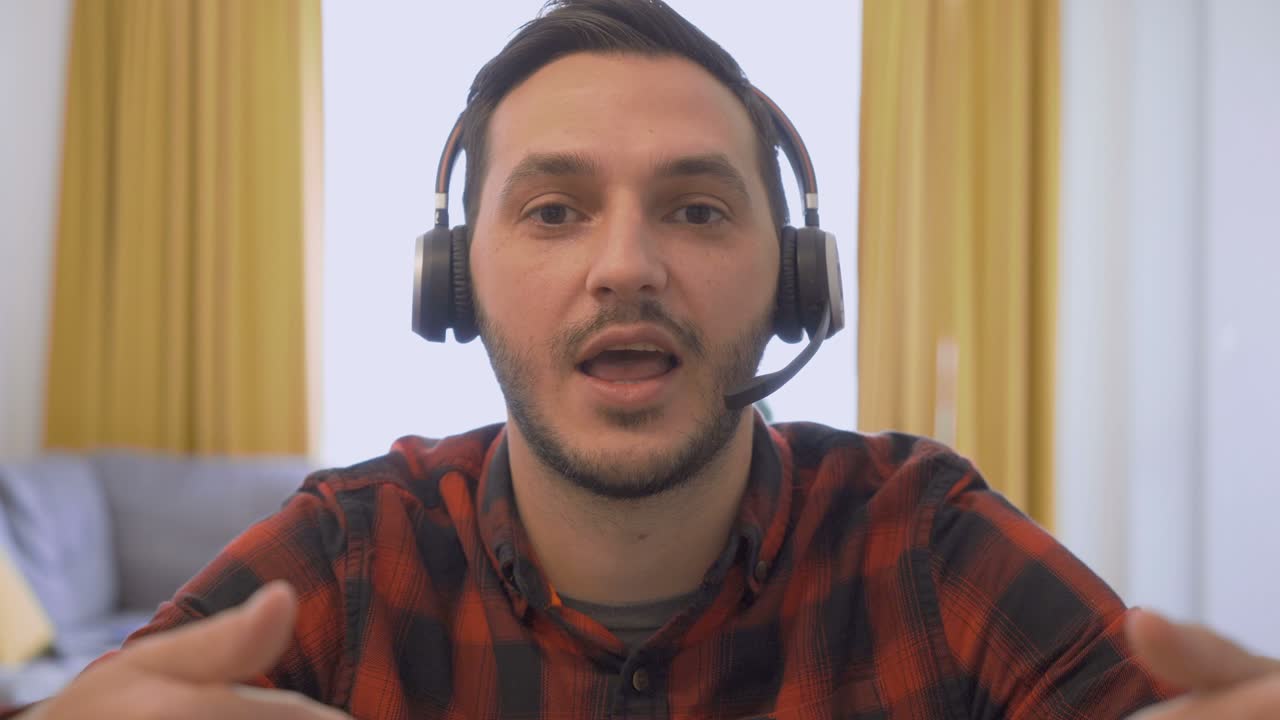 POV shot of handsome young man in wireless headset sitting in front camera and talking with client on video call