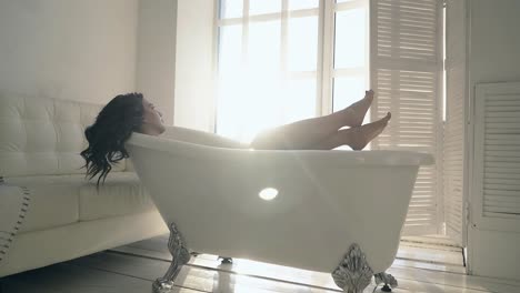 brunette girl with bare feet lies in retro bath in room