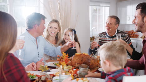 multi-generation family sitting at table making a toast whilst eating thanksgiving meal at home together