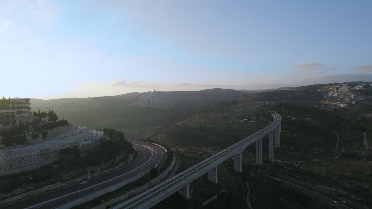 Enorme ponte ferroviario per passeggeri all'ingresso di Gerusalemme, Israele, sopra la Valle del Cedron - il treno moderno arriva da Tel Aviv, ripresa con drone al tramonto.