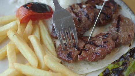 primer plano de un plato de albóndigas con papas fritas, tomate y pimienta verde.