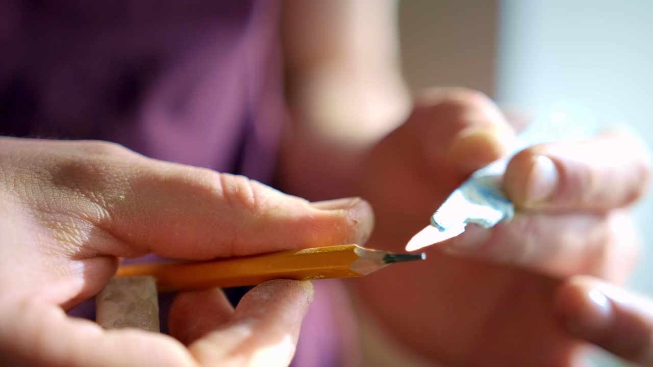 A close-up view of hands delicately preparing a sharpened pencil and a tube of adhesive, highlighting the intricate details and craftsmanship involved in a creative process