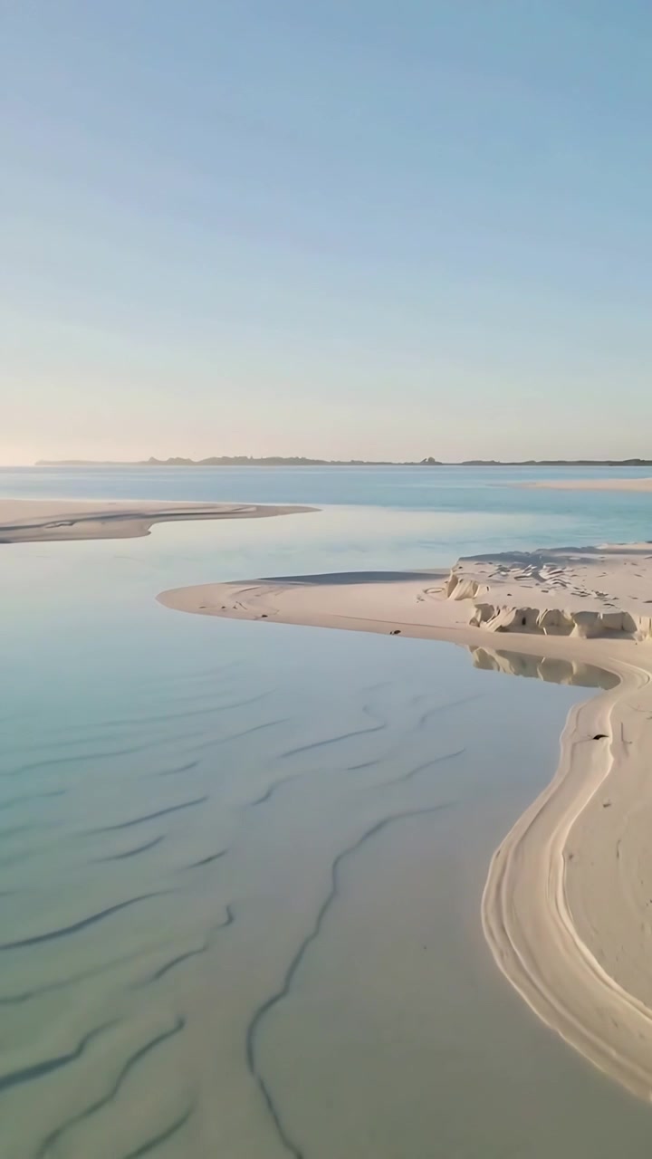 Lodret video: Svævende kamera viser sandbanke og blå kanal ved en tidevandsflade for kystdetaljer.