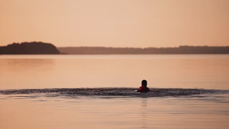 boy swimming in the river at sunset. silhouette of a child is splashing happily in the evening water outdoors. slow motion.
