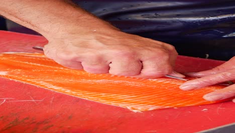 man filleting salmon on a red cutting board