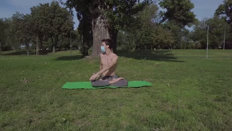 hermoso joven en forma con máscara practicando yoga en el parque, hombre moreno haciendo ejercicio y pasando tiempo activo