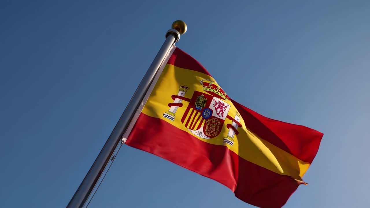 Low-angle shot of the Spanish flag waving against a clear blue sky, capturing a sense of pride