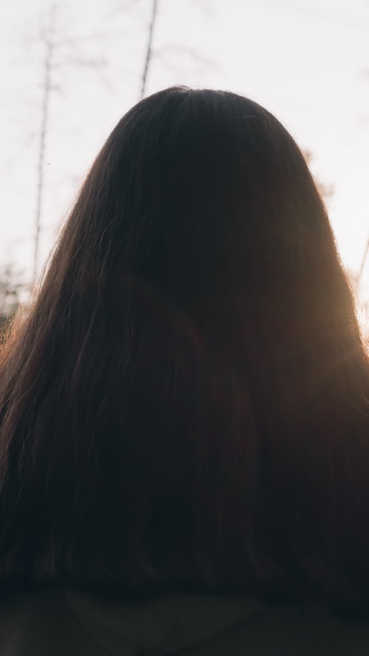 긴 느슨한 머리카락을 가진 여자가 해가 지는 동안 숲에서 산책합니다. 젊은 여자는 밀집한 나무의 전망을 즐기고 개인적인 문제에 대해 생각합니다.