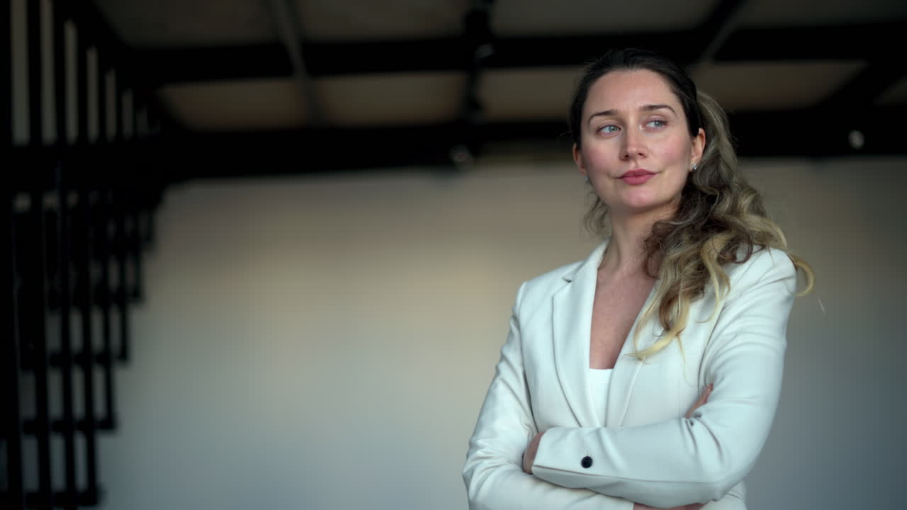 A professional woman in a white blazer standing confidently with crossed arms, conveying leadership and determination
