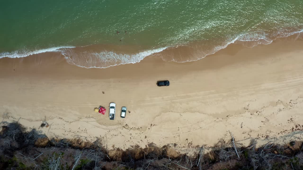 Aerial drone birds eye top view shot following a car drying down the tropical Malemb&aacute; beach with golden sand and calm crystal clear turquoise water near Tibau do Sul in Rio Grande do Norte, Brazil