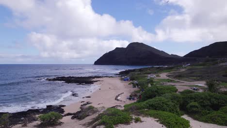 drone footage along a sandy hawaiian beach on the island of oahu as ocean waves roll calmly to shore with lush greenery lining the secluded beach