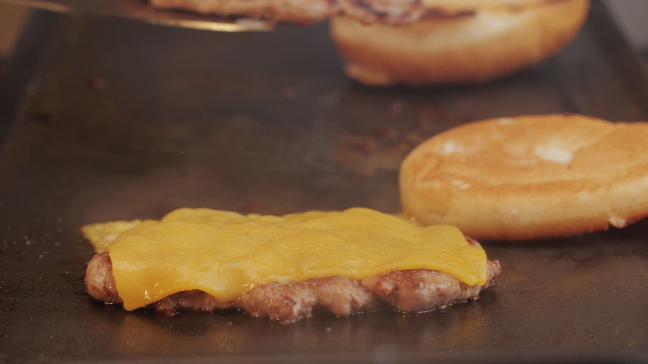 Cooking American fat smash burger with cheese slice on top on grill close-up. Beef or pork cutlet smashing by burger press. The chef in kitchen of the restaurant making cutlets for burgers - smash burger beefsteak. Fast and street food concept.