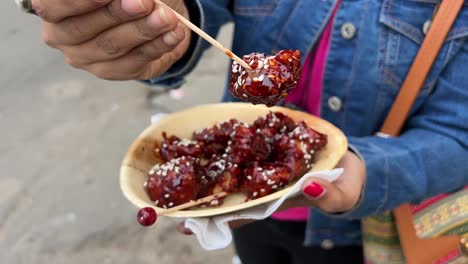 fotografía de cerca de una mujer comiendo pollo crujiente picante de corea del sur con palillos de dientes de un puesto en la carretera en calcuta, india