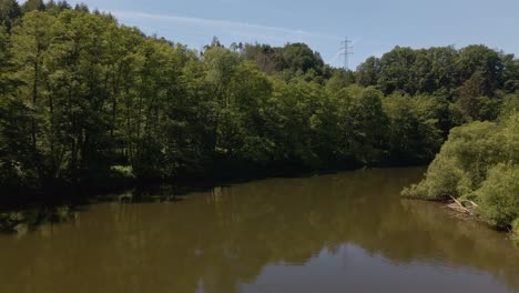 Wide-angle-drone-footage-following-a-meandering-brown-river-in-between-lush-green-banks-covered-by-thick-deciduous-forests-and-bushland