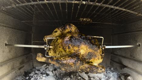 rotisserie chicken rotating in a wood and charcoal fire brick bbq grilling in slow motion