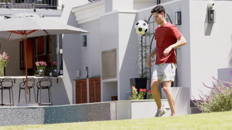 Hombre-Birracial-Enfocado-Haciendo-Malabarismos-Con-El-Fútbol-Con-Muslos-En-Un-Jardín-Soleado,-Espacio-Para-Copiar,-Cámara-Lenta