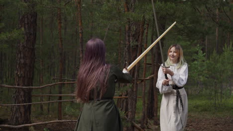 teenage girls in elegant clothes fight on swords at camp