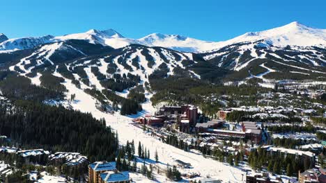 Giant-Ski-Resort-with-People-Skiing-and-Riding-Chairlifts-Down-Mountain-Slopes-through-a-Pine-Tree-Forest-Covered-in-Snow,-Aerial-Drone-View