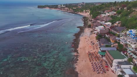 overhead drone clip moving forward, following the sandy shoreline of bingin beach, bali, indonesia with coral reefs and clean ocean water