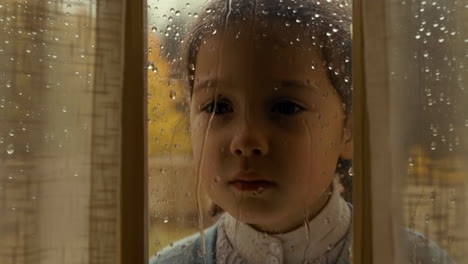 young girl looking out a rainy window