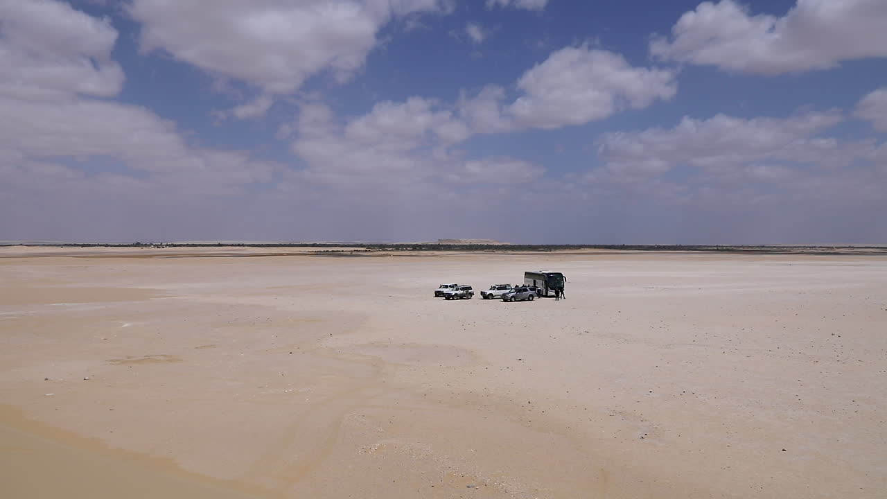 Cars walking on the sand and others parking under a cloudy sky in the desert - wide shot