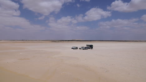 cars walking on the sand and others parking under a cloudy sky in the desert - wide shot