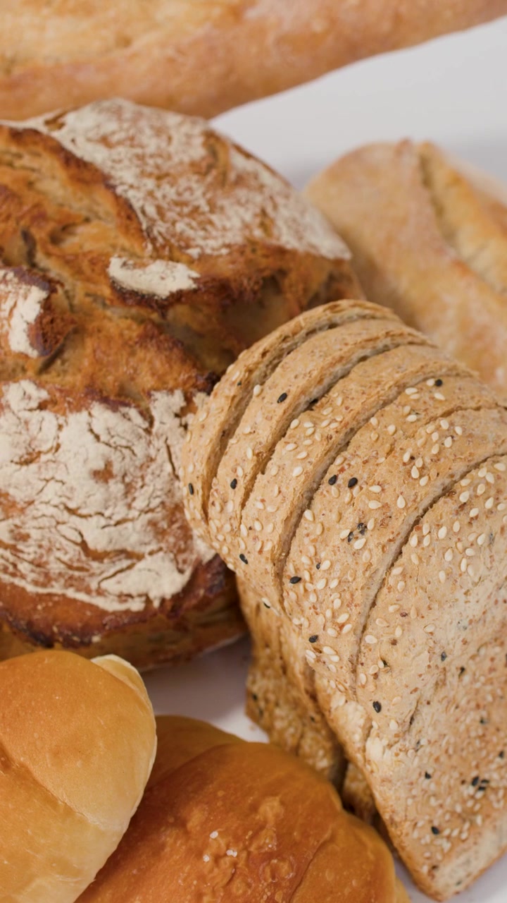 Zoom ravvicinato della telecamera su una varietà di pane a lievitazione naturale croccante, pagnotte affettate e croissant dorati.