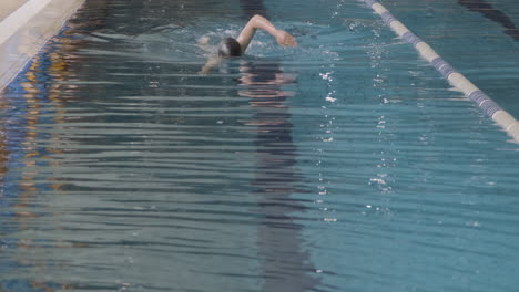 Frontale-Aufnahme-Einer-Jungen-Schwimmerin-Mit-Mütze-Und-Schutzbrille,-Die-In-Einem-Hallenbad-Kraulschwimmen-Schwimmt