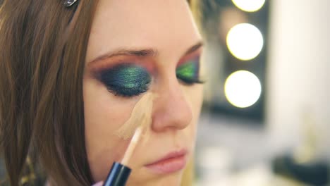 makeup artist applying foundation on young woman's face using brush putting it on a nose and cheek. side view