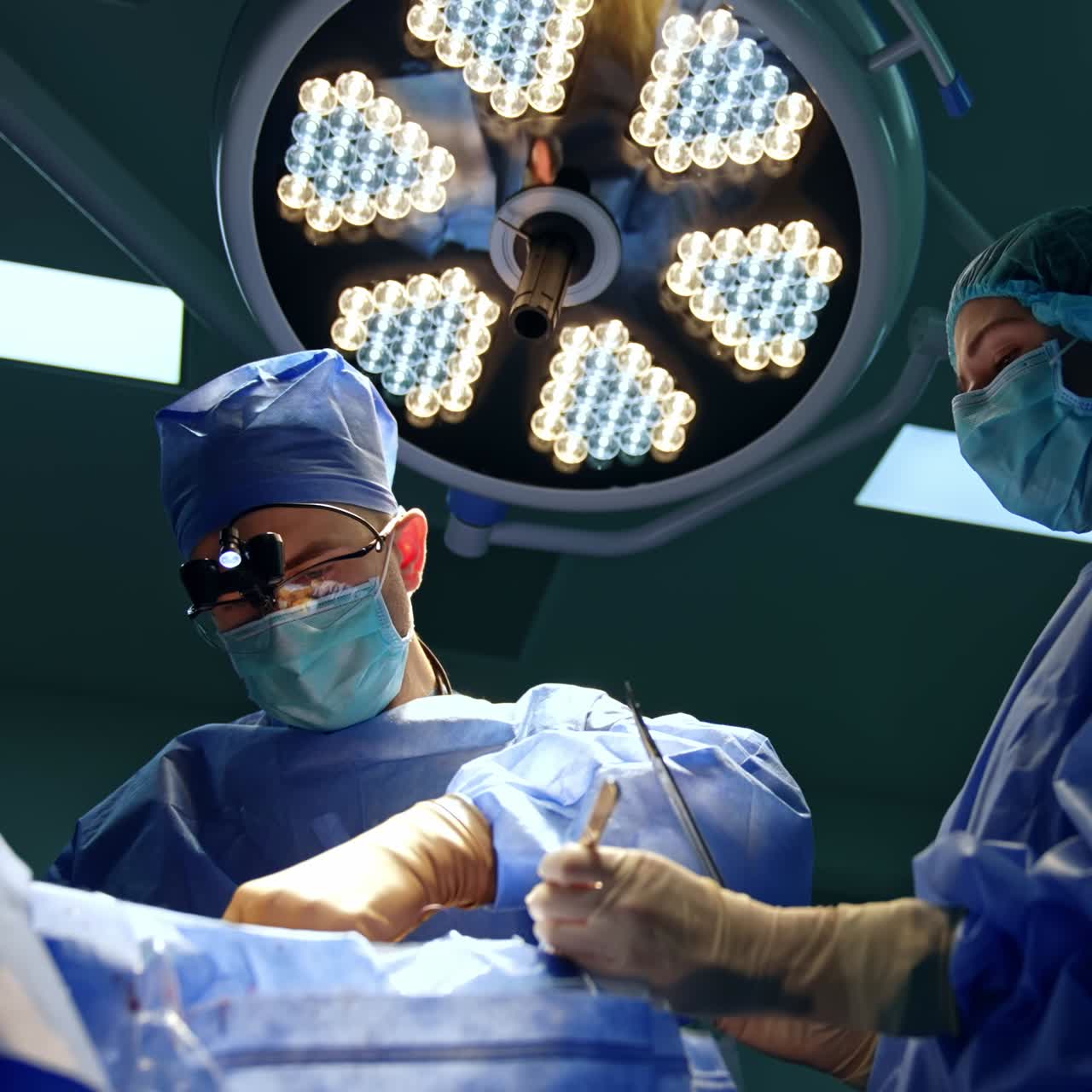 Focused neurosurgeon performing operation under the round lamps in surgery room. Female doctor assisting. Low angle view