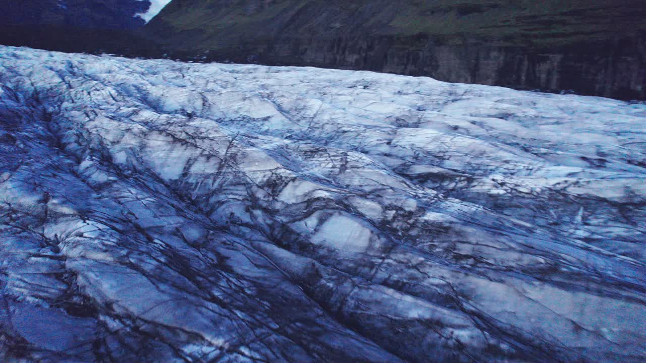 Aerial: Reverse of glacier's serpentine path with deep crevasses and jagged ice formations, evidence of the impact climate change has on the constant movement and transformation of this natural wonder