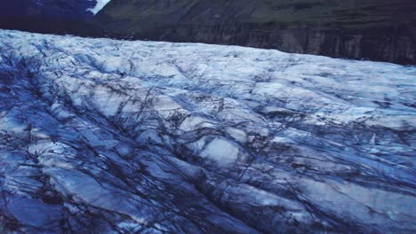 Aerial:-Reverse-of-glacier's-serpentine-path-with-deep-crevasses-and-jagged-ice-formations,-evidence-of-the-impact-climate-change-has-on-the-constant-movement-and-transformation-of-this-natural-wonder